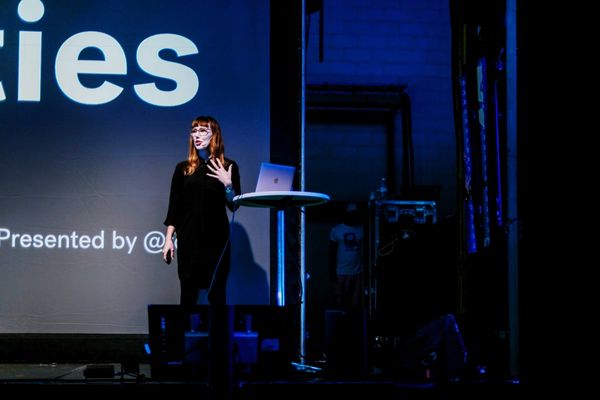 Karolina speaking at Nordic.js in Stokholm. She's on stage next to a lectern with a laptop. She's wearing all black and gesticulating with an open hand. In the backround, there's a fraction of the introductory slide to her talk.