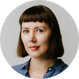 Portrait of Karolina on a grey background. She's slightly smiling, looking into the camera, wearing a light blue shirt.