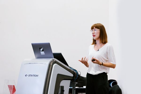 Karolina speaking at Creative Mornings in Melbourne. She's standing behind a lectern with a laptop, holding a remote to switch slides. She's mid-speaking, but not in a bad way. She's wearing white t-shirt and black pants.