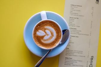 Interior of Beautiful Jim Keys café. Latte with a leaf rosetta in a pale blue cup, shot from above on a yellow table beside a drinks menu.